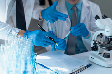 Scientists in protective gear examining blue liquid test tubes, documenting findings with microscope while conducting medical laboratory research