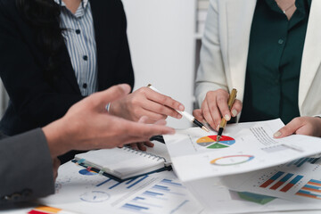 Business team analyzing financial charts and discussing data in office meeting using documents and notepad
