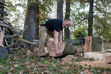 Man lifting heavy firewood in autumn forest.