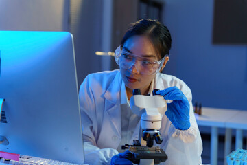 Asian female scientist using microscope and computer, performing scientific research in a laboratory