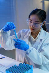 Scientist wearing lab coat and protective glasses pouring blue liquid substance in test tube during...