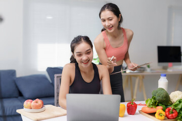 Asian nutritionist coaching a woman about healthy eating habits, using a laptop and pointing to a clipboard with healthy food on the table