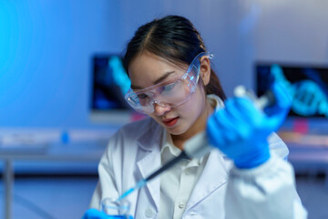 Female scientist in protective gear carefully pipetting liquid into test tube, scientific workspace...