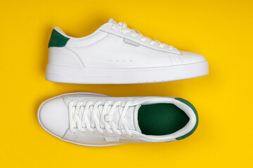 Pair of stylish white sneakers on yellow background