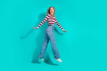 Young woman jumping in casual striped sweater on turquoise background expressing joy and happiness
