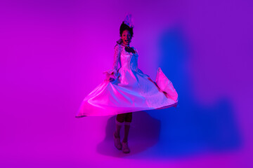 Elegant young woman in glamorous lace gown dances joyfully under vibrant neon lights, capturing the essence of a modern masquerade