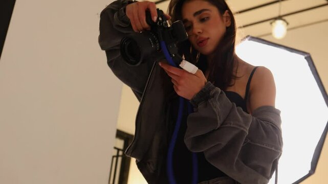 An girl artist prepares their camera in a stylish studio filled with lighting equipment. The focus is on setting up for a creative shoot that promises artistic visuals.