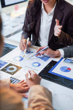 Businesswomen pointing at financial charts and discussing data during a meeting, analyzing company performance and planning strategies
