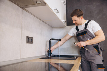 Plumber fixing kitchen faucet in modern apartment