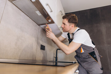 Plumber repairing extractor hood in kitchen using screwdriver