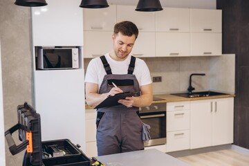 Plumber writing notes on clipboard in kitchen during maintenance service