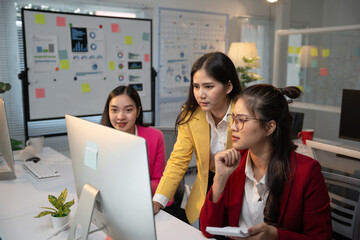 Three Asian businesswomen are collaborating on a project, analyzing data on a desktop computer in a modern office environment