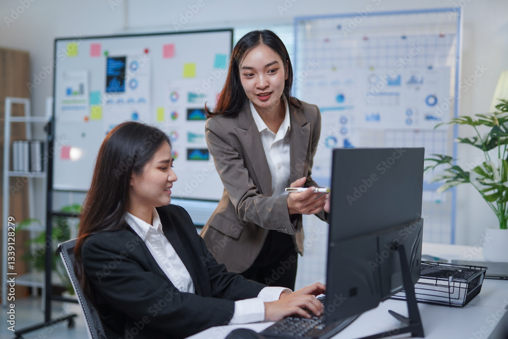 Poster two asian businesswomen engaging in a discussion about a new project while collaborating at a deskto