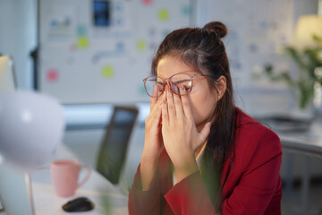 Asian office employee having painful eye strain, massaging her eyes after long computer work, suffering from dry eye syndrome, bad vision, tired businesswoman
