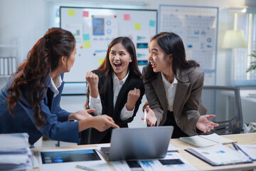 Group of asian businesswomen celebrating successful project while looking at laptop in office