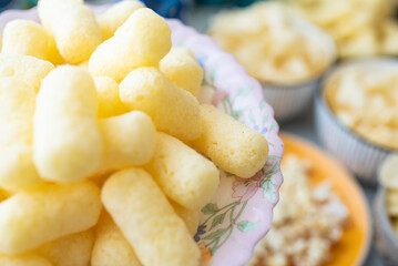 sweet corn sticks on yellow plate, plate on background of bowls with various snacks on table