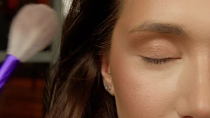 Makeup artist applying shimmering eyeshadow on model's eyelid, using delicate professional brush with meticulous precision during beauty makeover