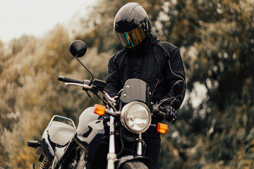 Male motorcyclist in leather jacket and helmet on classic motorcycle outdoors