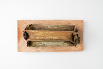 Fototapeta premium Lontong or rice cake on wooden plate. Traditional Javanese food made from steamed rice and wrapped in banana leaves. Isolated on white background, flat lay setup