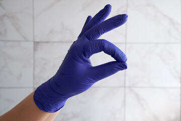 Hand in medical glove showing OK. On gray background.