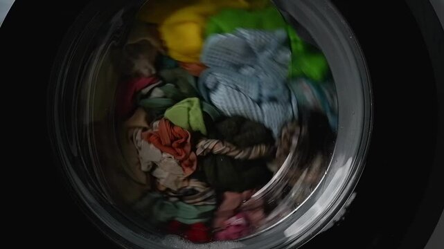 Colorful clothes are spinning inside washing machine drum