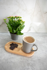 A cup of coffee and a piece of black chocolate near the green flower. Morning routine
