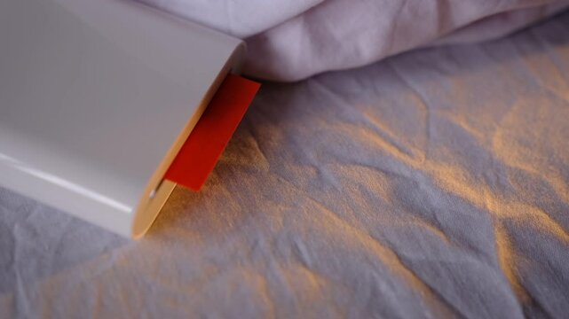 A compact pocket-sized white printer on bed prints polaroid style photo with orange colour in minimalist design modern technology creative process cozy atmosphere vibrant details portable convenience