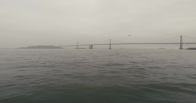 Suspension bridge straddling over a strait covered with dense fog during a cloudy daytime