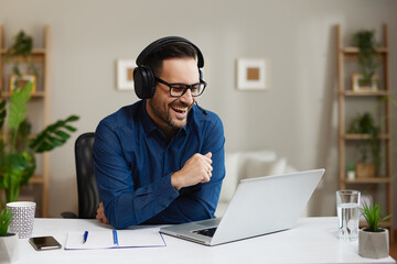 Obraz premium Businessman wearing headset working from home office having a video conference on laptop and laughing