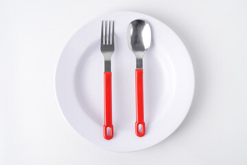 Empty white colored round shaped plate, red handle spoon and fork. Isolated on white background. Flat Lay Setup