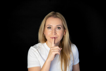 portrait of a beautiful blonde woman smiling and showing sign hands for shut up. Isolated on black...