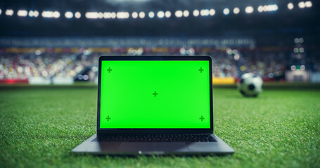 Laptop Computer with Green Screen Mock Up Display with a Soccer Ball Rolling in the Background on a Stadium Field at Night. Template for Software, Streaming, Sports Betting, Multimedia Content