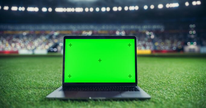 Laptop Computer with a Green Screen Mock Up Display on a Soccer Stadium Field at Night. Template for Software, Streaming, Sports Betting, Multimedia Content and Social Media Management - Powered by Adobe