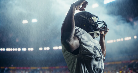 Powerful Portrait of an African American Football Player, Celebrating on the Field Under Stadium Lights in Rain. Intense and Inspirational Sports Photo with Dramatic Lighting and Weather Conditions © Gorodenkoff