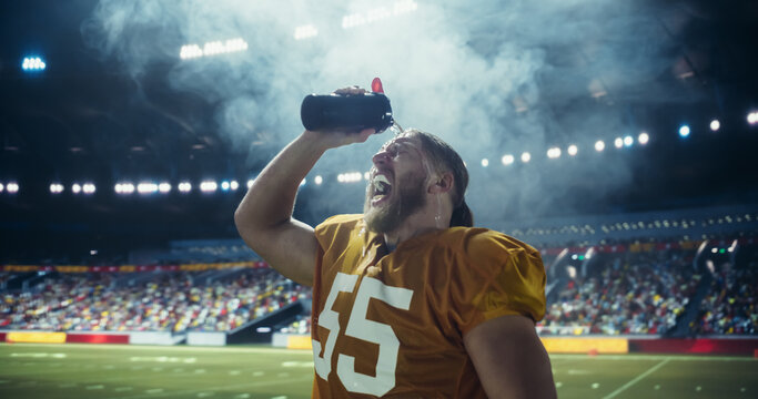 American Football Player Pouring Water on His Face During Championship Game in Stadium. Male Athlete Hydrating on Field with Crowd in the Background. Professional Sportsmen Drinking Water - Powered by Adobe
