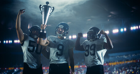 Diverse American Football Team Members Raise the Championship Cup. Happy College Team Standing Under Stadium Lights, Celebrating a Triumphant Victory in Front of a Crowded Stadium with Fans