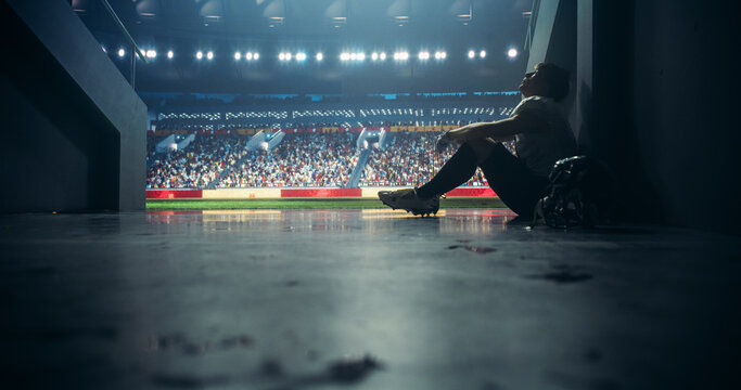 American Football Player Sitting Alone in a Stadium Tunnel, Tossing Away His Helmet. Background with a Crowded Stadium with Sports Fans. Footballer is Emotional Devastated After Championship Game