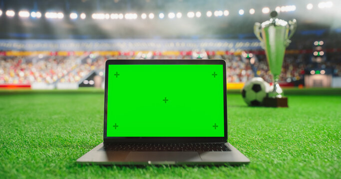 Laptop Computer with a Green Screen Template Standing on a Soccer Pitch with a Trophy and Soccer Ball in the Background. Mock-Up Display Suitable for Adding Sports-Themed Digital Content