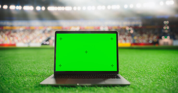Laptop Computer with a Green Screen Mock Up Display on a Soccer Stadium Field at Night. Template for Software, Streaming, Betting, Multimedia Content and Social Media Management - Powered by Adobe