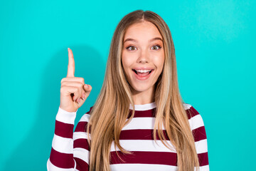 Excited young woman pointing upwards against turquoise background wearing stylish striped pullover