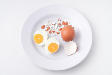 Someone cracks the shell of a boiled egg, peels it, and places it on a white plate. Isolated on white background