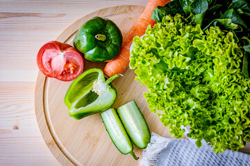 Fresh organic vegetables on a wooden cutting board. Green bell pepper, lettuce, cucumber, tomato, and carrot create a vibrant and healthy food concept. Ideal for diet, nutrition, and culinary themes