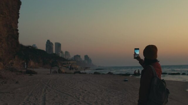 Travel to Israel. Girl takes photos of the city and the beach on her phone for social networks. Sunset on the beach. beach in Netanya. Travel and content creation. Netanya. Israel.