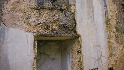 A close-up of a deteriorating concrete bunker wall shows deep cracks, exposed aggregate, and rusted reinforcements. Water drips from the damaged overhang above an empty, shadowed alcove.