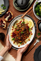 Top view of Moroccan style Lamb and  Chickpea Stew, served with pomegranate, coriander and couscuos. Hands holding a plate with festive food, vertical image.