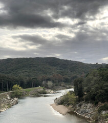 A serene river winding between forested hills beneath a dramatic, overcast sky