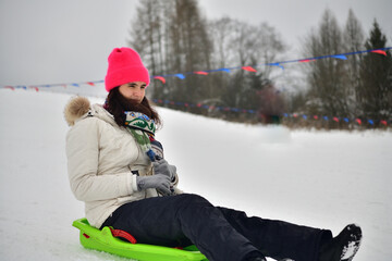 Girl sledding downhill on snow in winter and laughing with joy