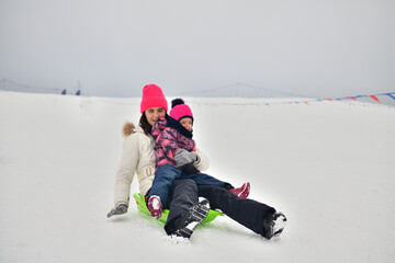 Two girls are tobogganing downhill on snowy hill in winter 