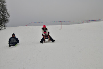 Family tobogganing down a snowy hill during winter vacation