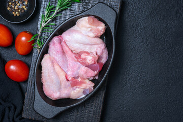 Raw chicken wings in a black cast iron pan on a dark textured background. Fresh ingredients include...